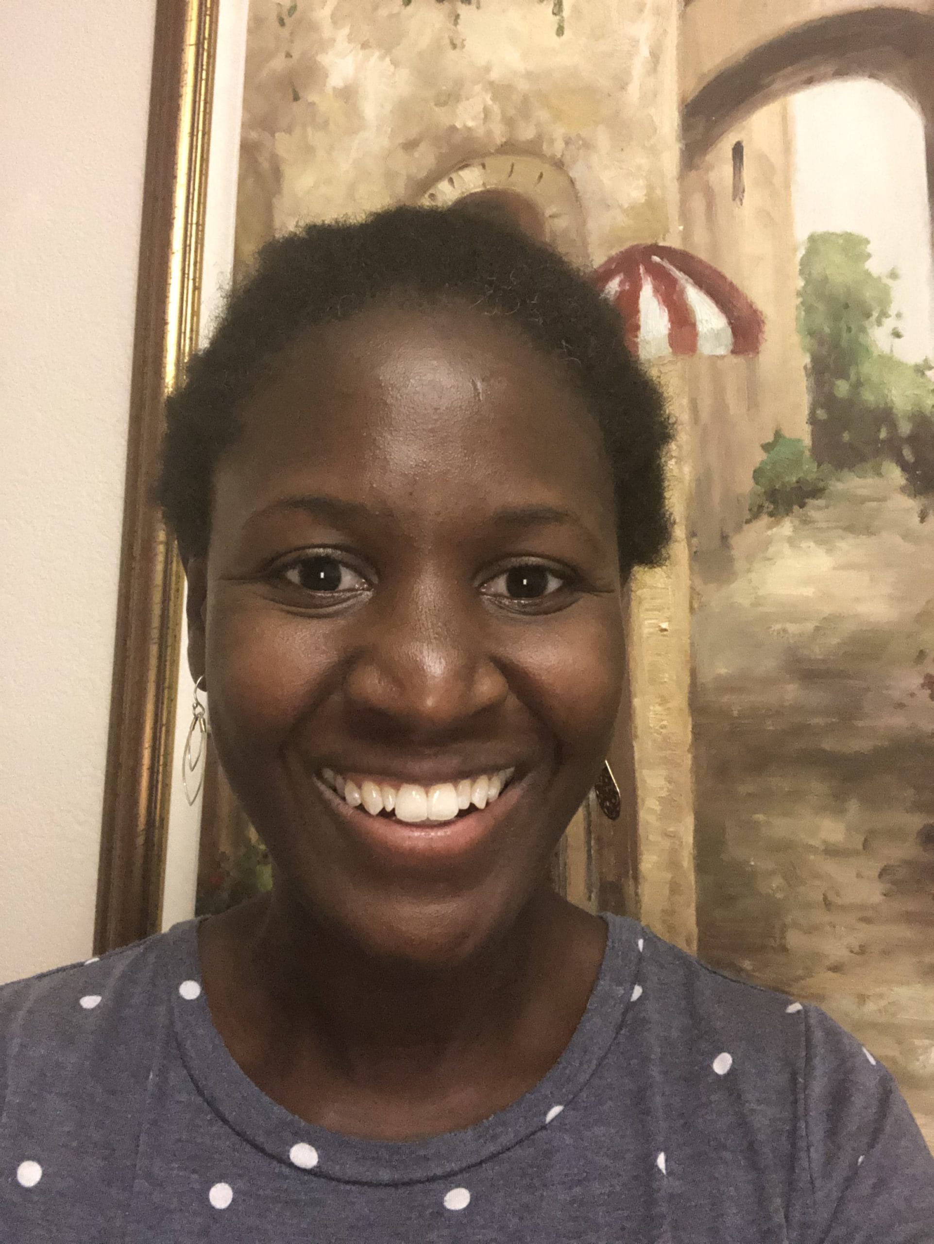 A woman smiling for the camera in front of a painting.