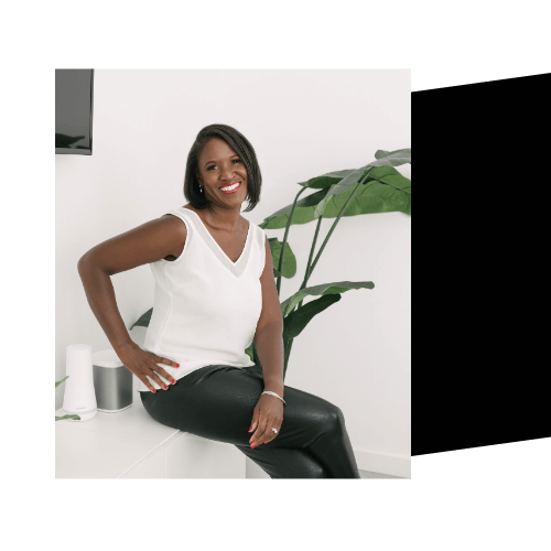 Denise Lee, life coach for entrepreneurs. She is sitting on top of a table in front of a plant.