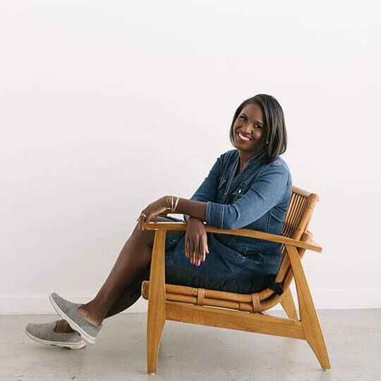 A woman sitting in a wooden chair smiling.