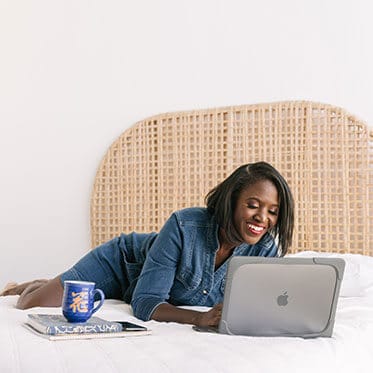 A woman laying on the bed looking at her laptop.