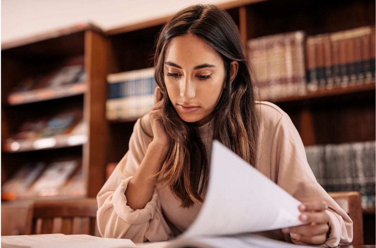 A woman sitting at a table looking down at papers.