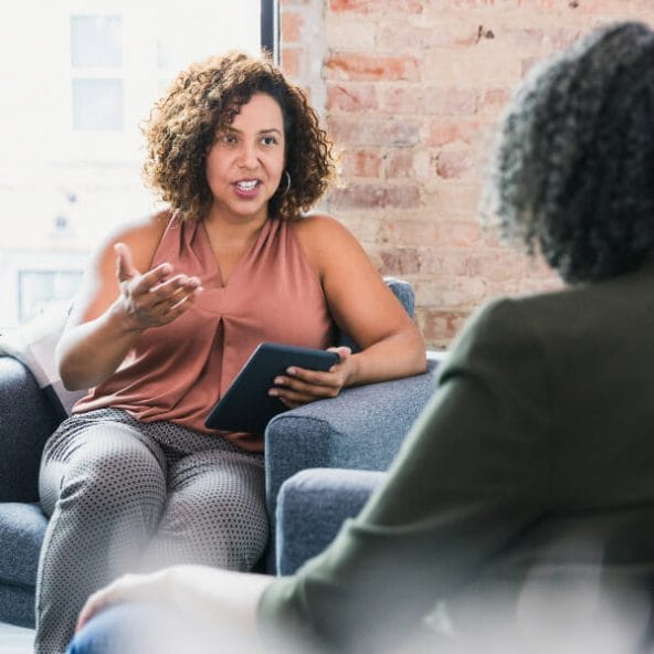 A woman sitting on top of a couch talking to another person.