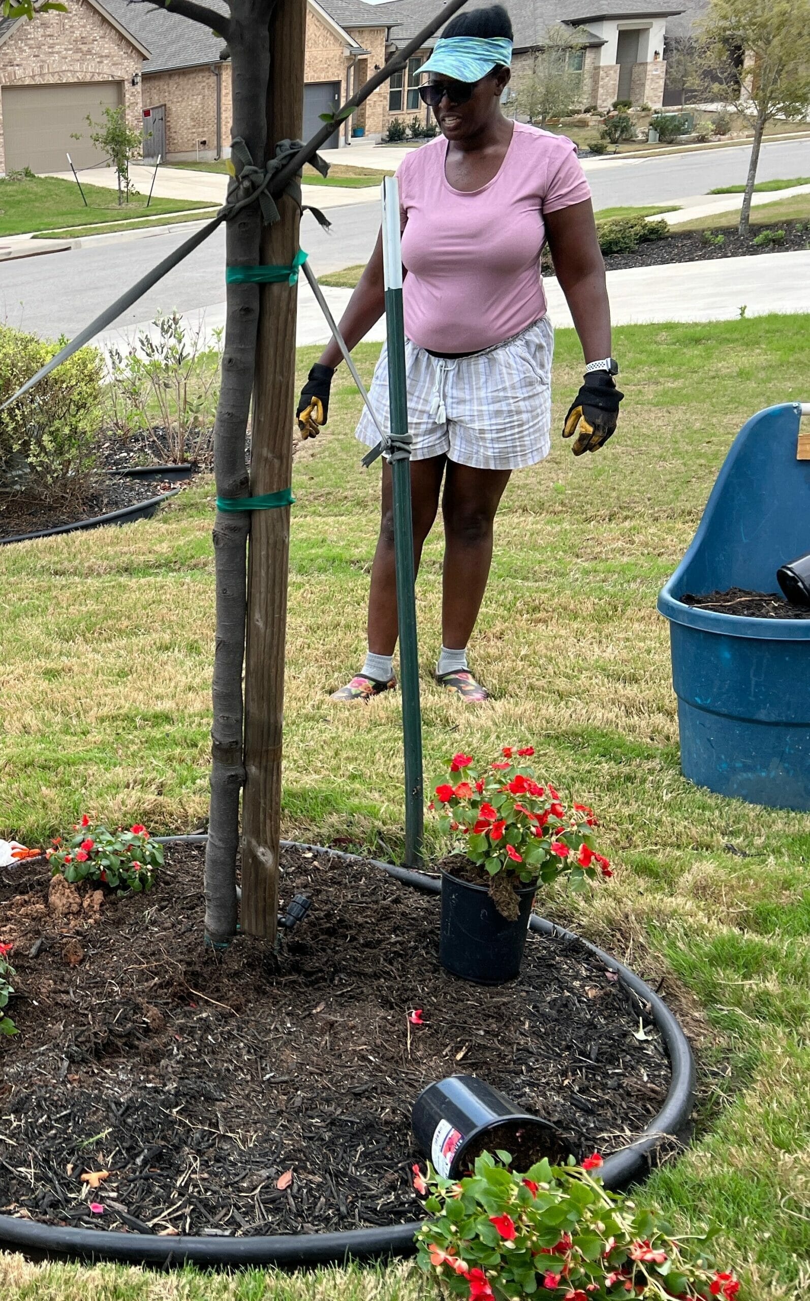 A woman in pink shirt and white shorts standing next to tree.