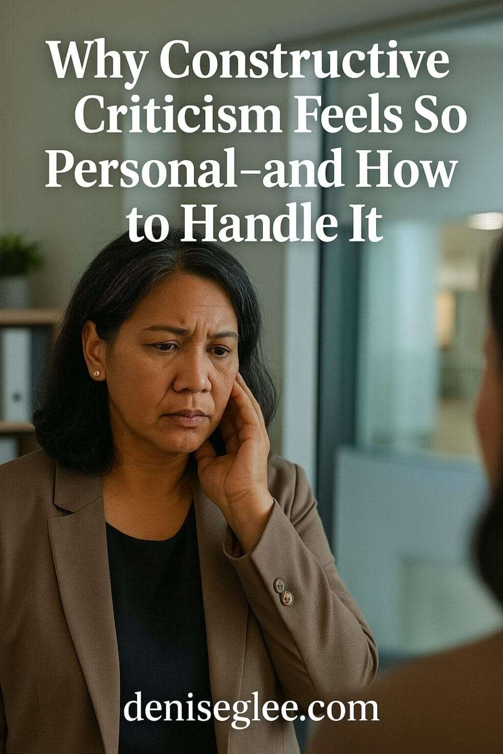 Pacific Islander woman in her 40s staring into a mirror at work, looking emotionally impacted—processing feedback in a professional setting