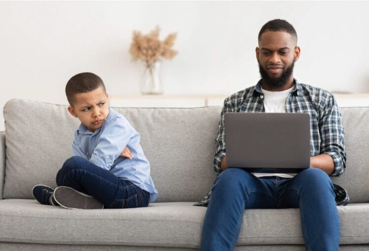 dad and son on couch. dad looking at his laptop