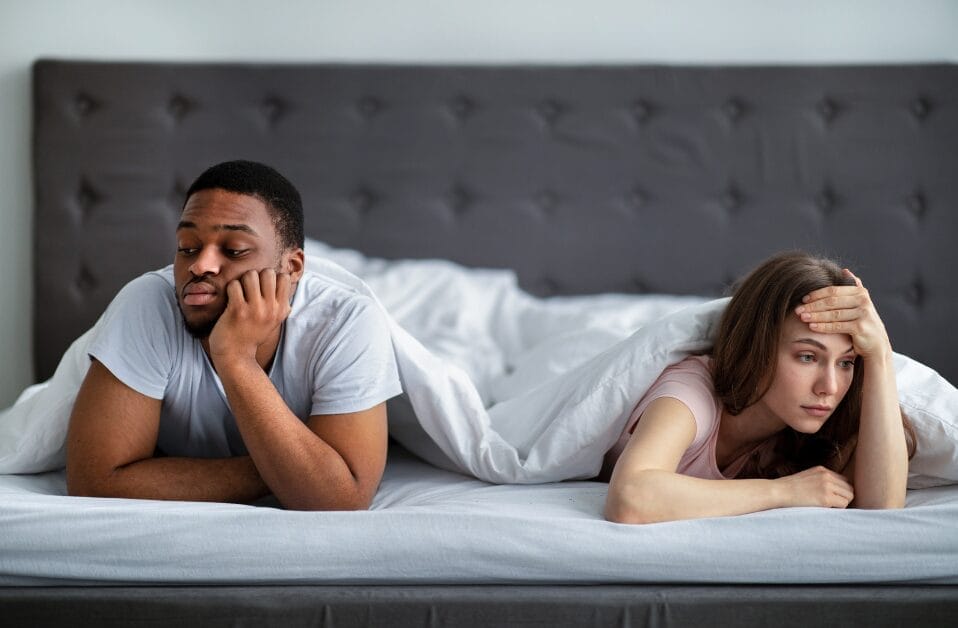 a couple in bed looking unhappy