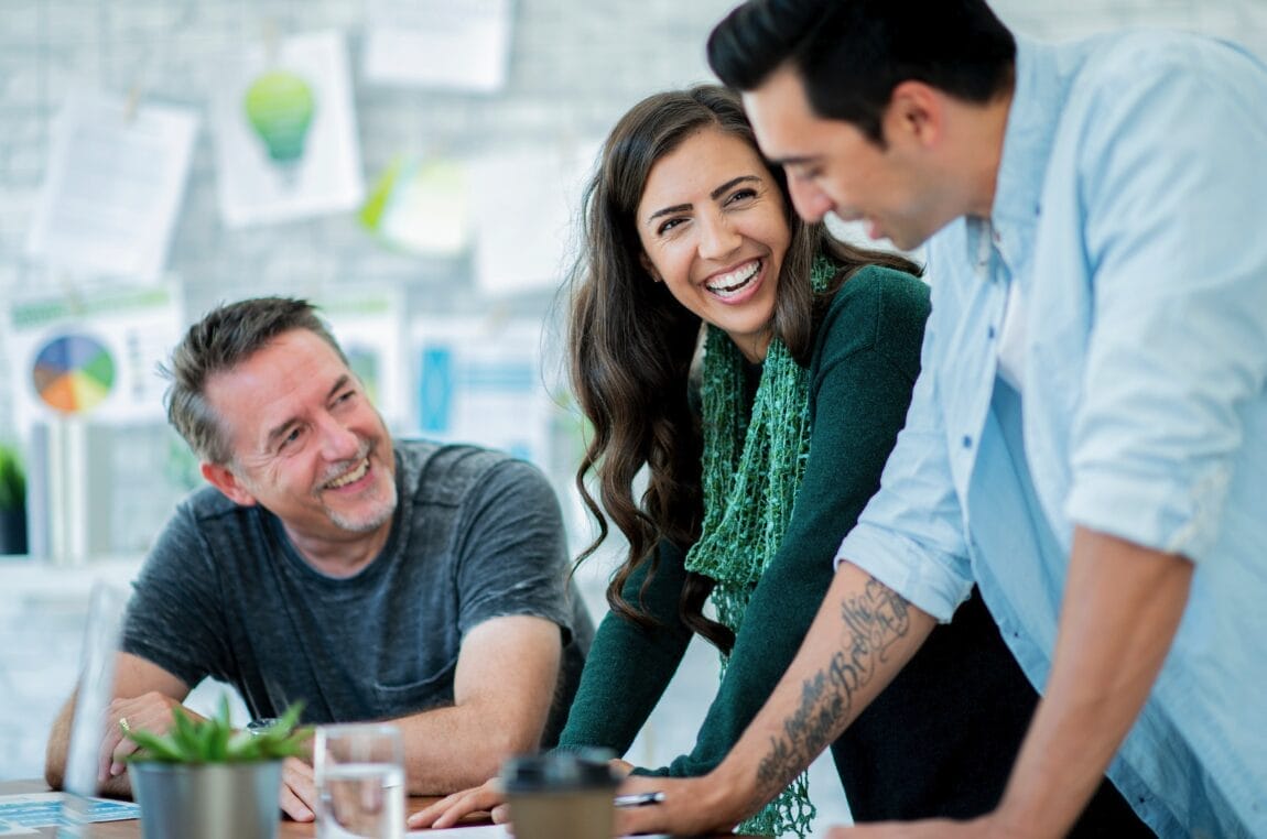 three people leaning at desk talking