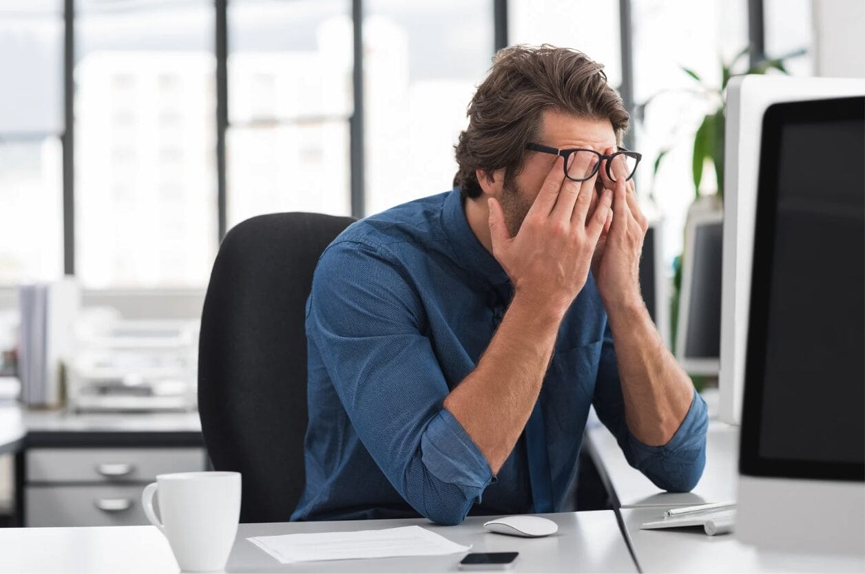 frustrated man at desk with his hand covering his face