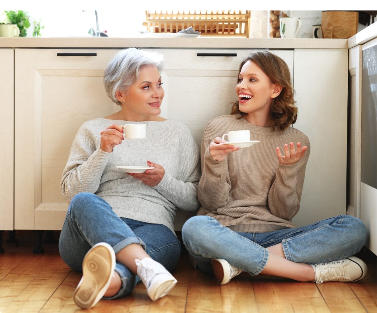 mother and daughter sitting on floor with drinks on their hands