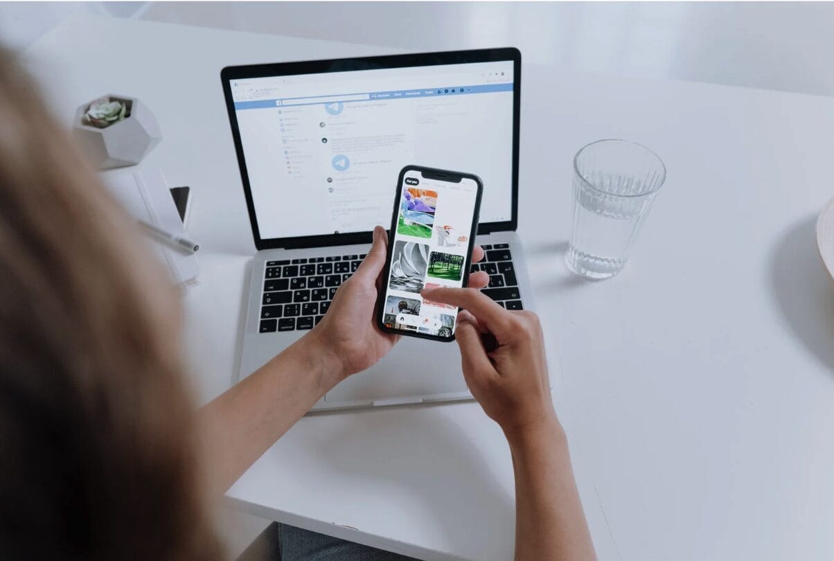 woman looking at phone while in front of laptop