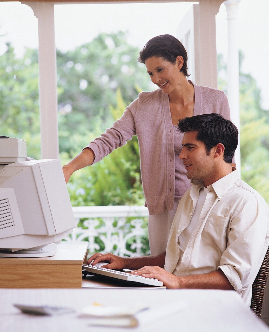 woman standing while looking at man type on computer