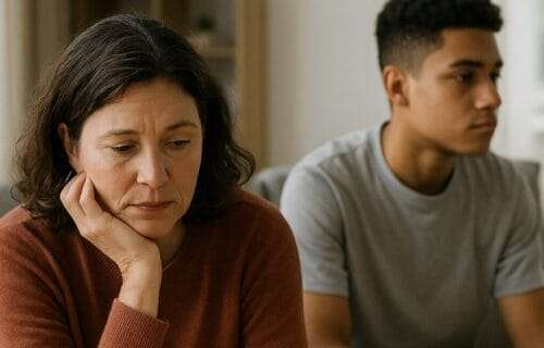 Concerned parent and withdrawn teen sitting apart on a couch, reflecting emotional distance