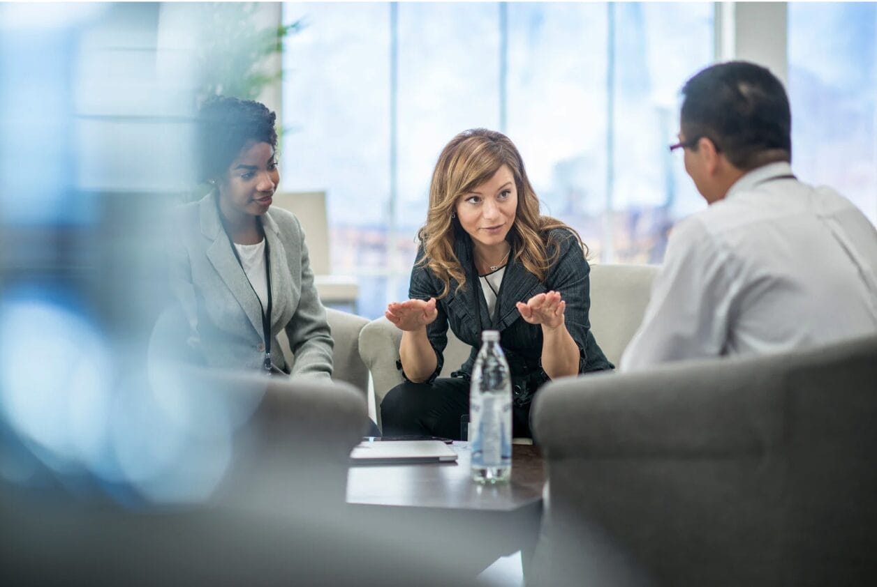 woman leader at desk talking with one man and women