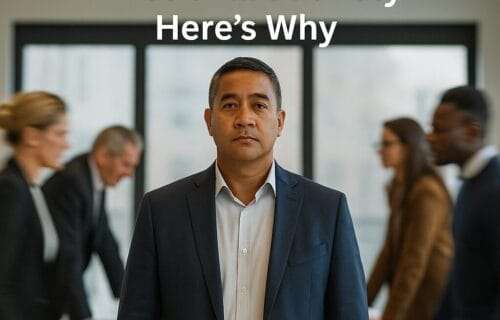 Pacific Islander man in his 40s standing calmly in a boardroom while others blur in motion around him