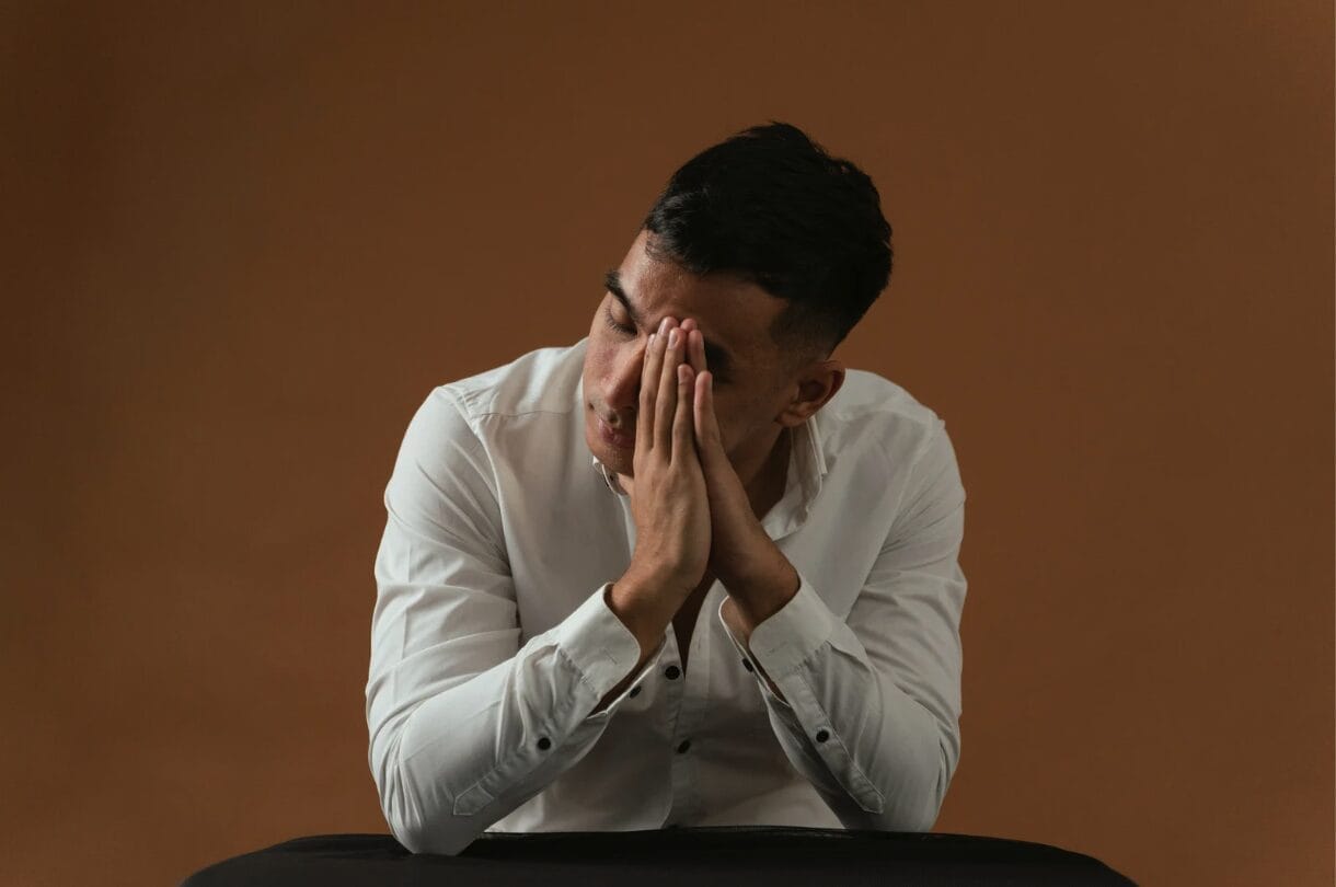 man with face cupped in hands with brown background