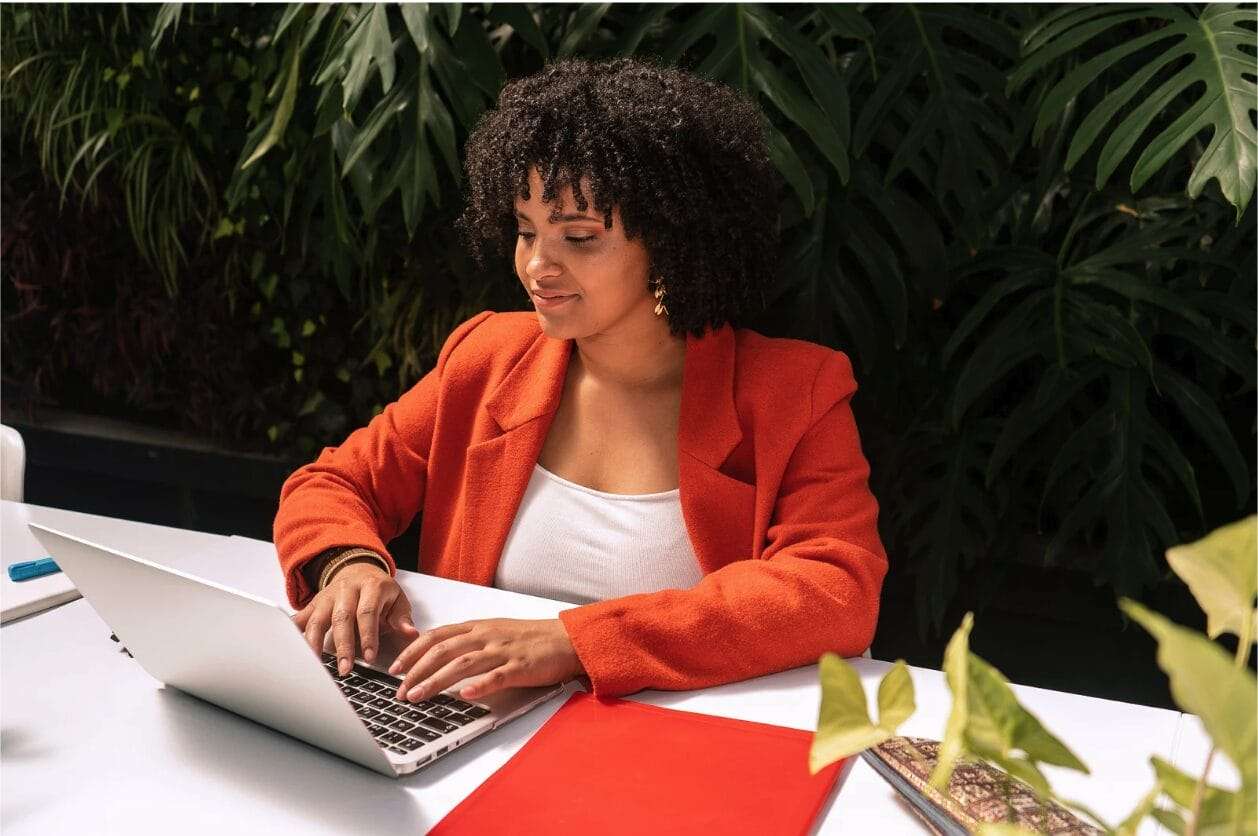 black woman with orange blazer typing on laptop