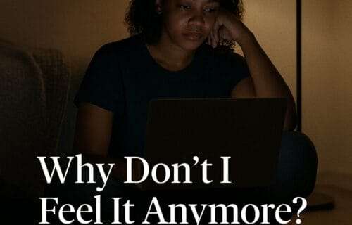 A young Black woman sits alone in a dimly lit room, illuminated by her laptop screen and a soft floor lamp, conveying emotional fatigue and introspection. Text reads: “Why Don’t I Feel It Anymore? The Quiet Grief of Emotional Numbness in Healers – deniseglee.com”
