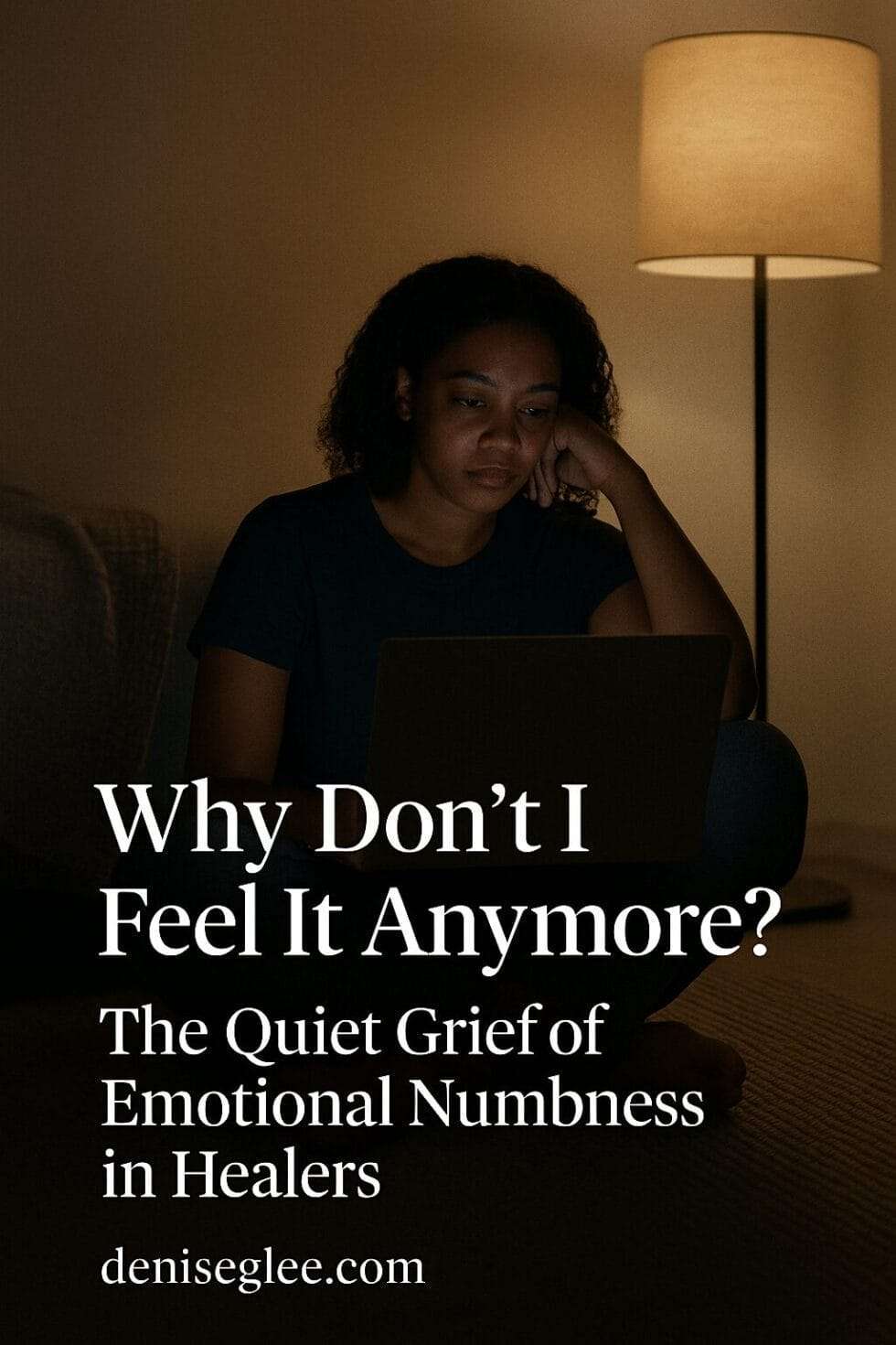 A young Black woman sits alone in a dimly lit room, illuminated by her laptop screen and a soft floor lamp, conveying emotional fatigue and introspection. Text reads: “Why Don’t I Feel It Anymore? The Quiet Grief of Emotional Numbness in Healers – deniseglee.com”