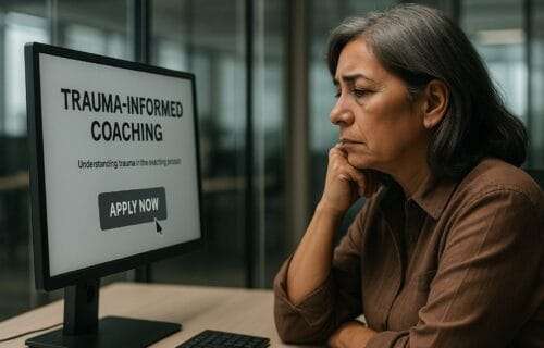 A middle-aged Latina woman sits at her desk in a modern glass office, staring at a computer screen showing a "TRAUMA-INFORMED COACHING" application. Her expression is tired and contemplative as the cursor hovers over the "Apply Now" button.