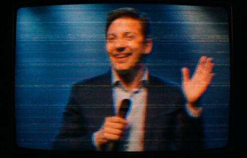 Distorted livestream image of a smiling speaker glitching on screen, symbolizing the tension between performance and authenticity.